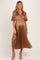 woman wearing a brown pleated maternity dress with short sleeves and a wrapped bodice, showcasing her baby bump
