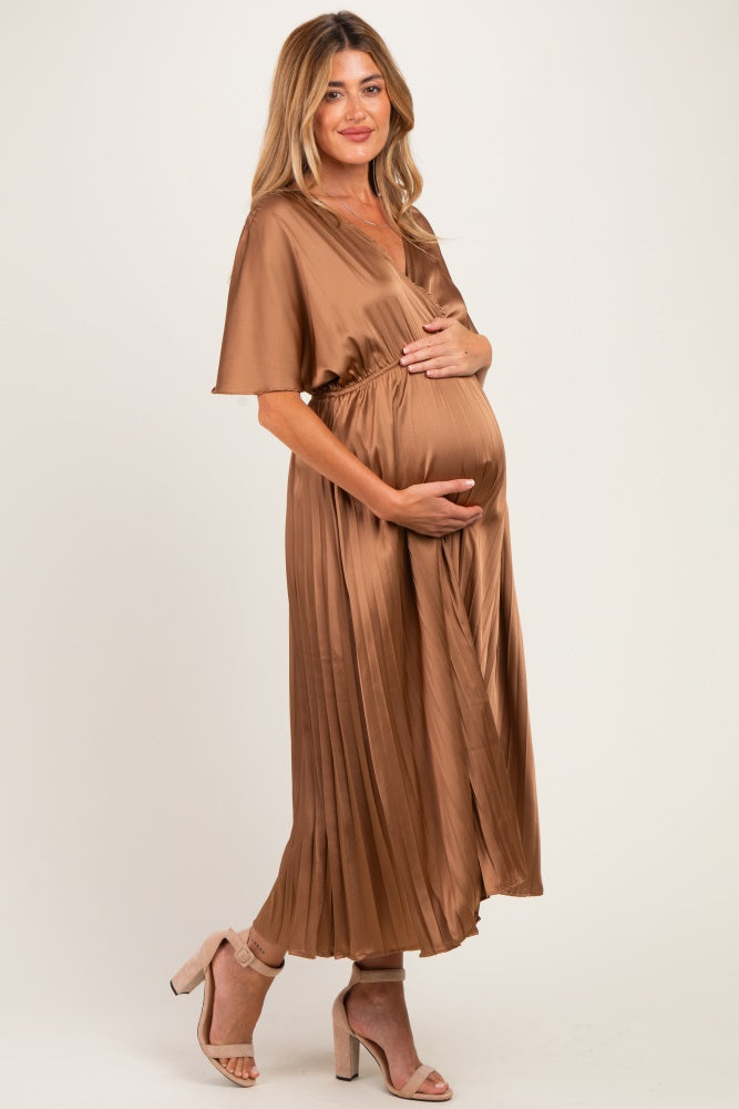 woman wearing a brown pleated maternity dress, showing her baby bump, standing in a relaxed pose