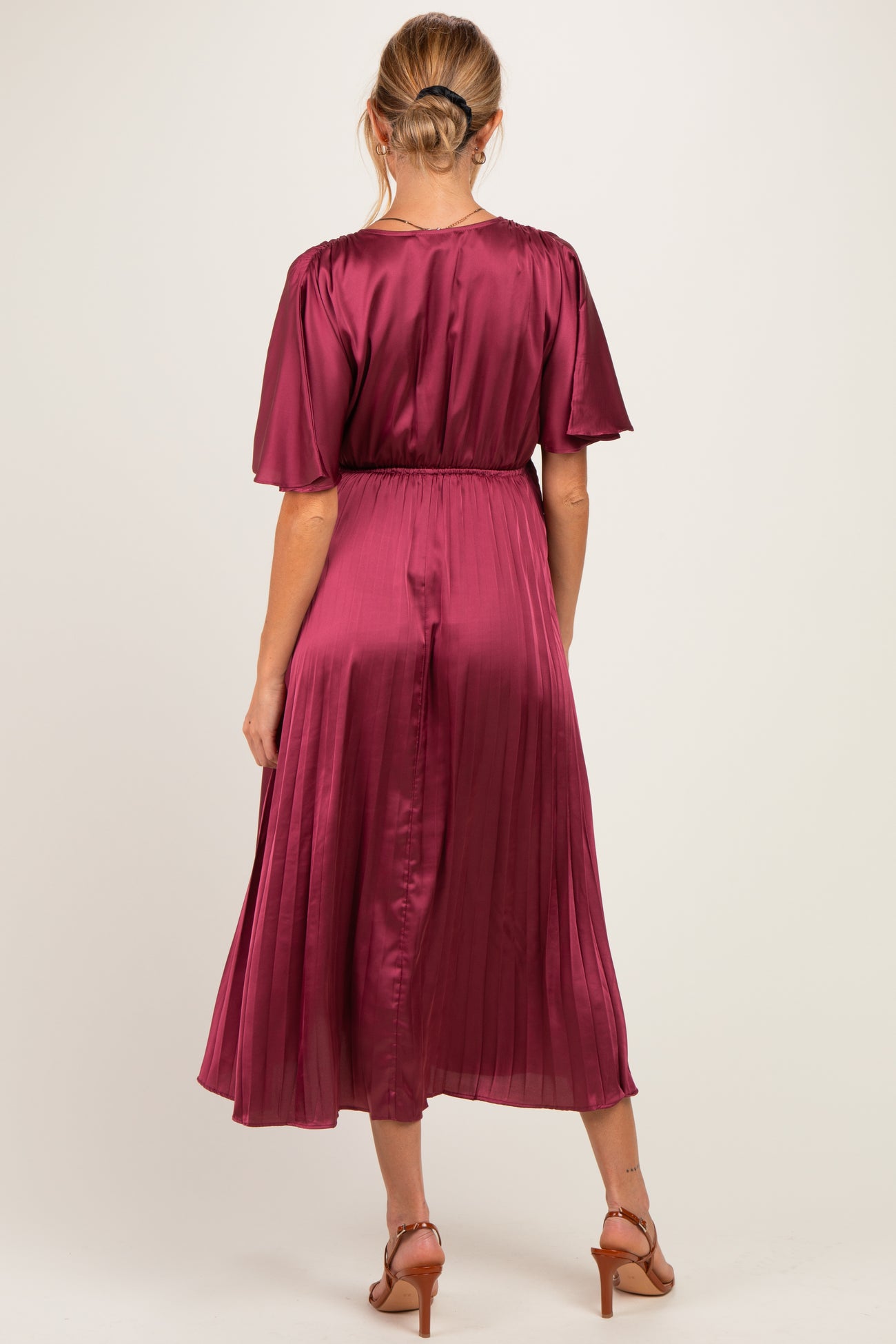 woman wearing a burgundy short sleeve pleated maternity dress, shown from the back