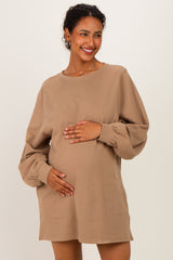 woman wearing a tan long sleeve maternity sweatshirt dress and holding her baby bump