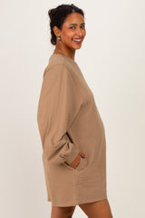woman wearing a tan oversized maternity sweatshirt dress with side pockets and a visible baby bump