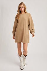 woman wearing a tan oversized sweatshirt dress with long sleeves and side pockets, paired with white cowboy boots