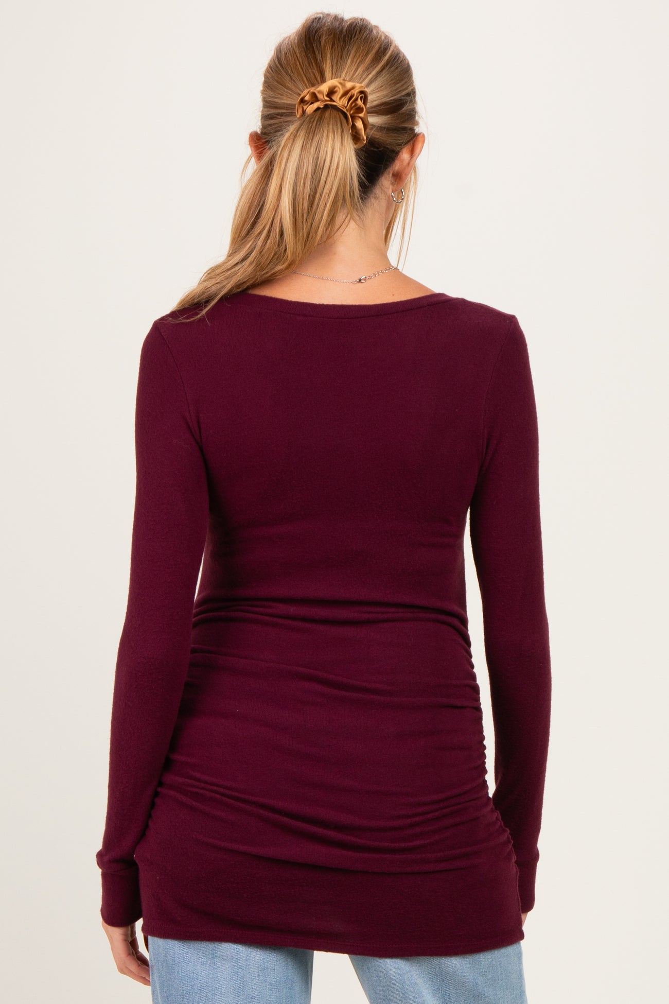 woman wearing a burgundy long sleeve maternity top with ruching detail at the waist