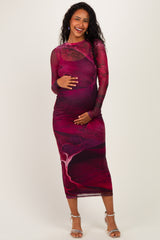 woman wearing a long sleeve maternity dress in a red and burgundy abstract design, gently holding her baby bump