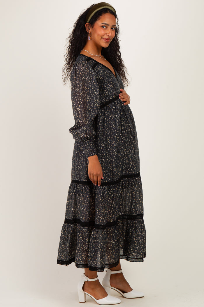woman wearing a black floral maternity dress with long sleeves and tiered design, showcasing her baby bump