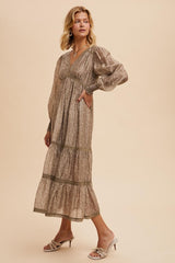 woman wearing a long beige floral maxi dress with puff sleeves and tiered skirt, posing with one hand on her hip