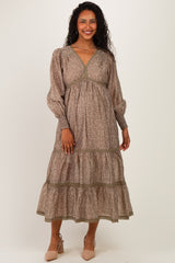 woman wearing a brown floral print maternity maxi dress with long sleeves and a tiered skirt, showcasing her baby bump