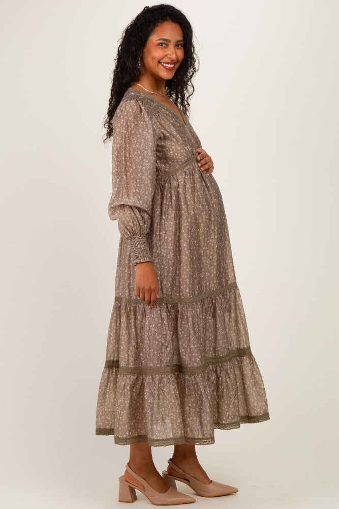 woman wearing a brown floral print maternity dress with tiered skirt and long sleeves, showcasing her baby bump
