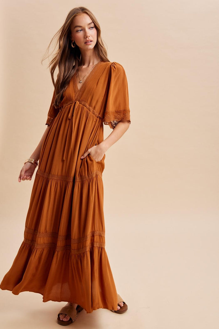 woman wearing a rust-colored tiered maxi dress with short sleeves and pockets, posing against a neutral background