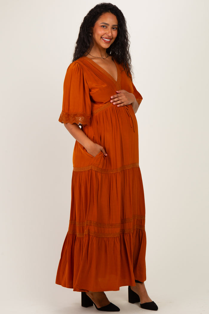 woman wearing an orange maternity maxi dress with a deep v-neck, short sleeves, and pockets, showing her baby bump