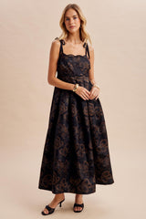 woman wearing a black floral print maxi dress with shoulder straps and a fitted bodice, styled with black heels