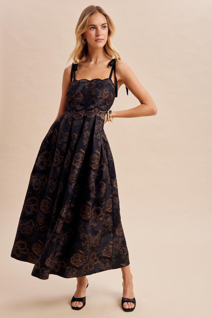 woman wearing a black floral print maxi dress with spaghetti straps and a fitted bodice, standing confidently