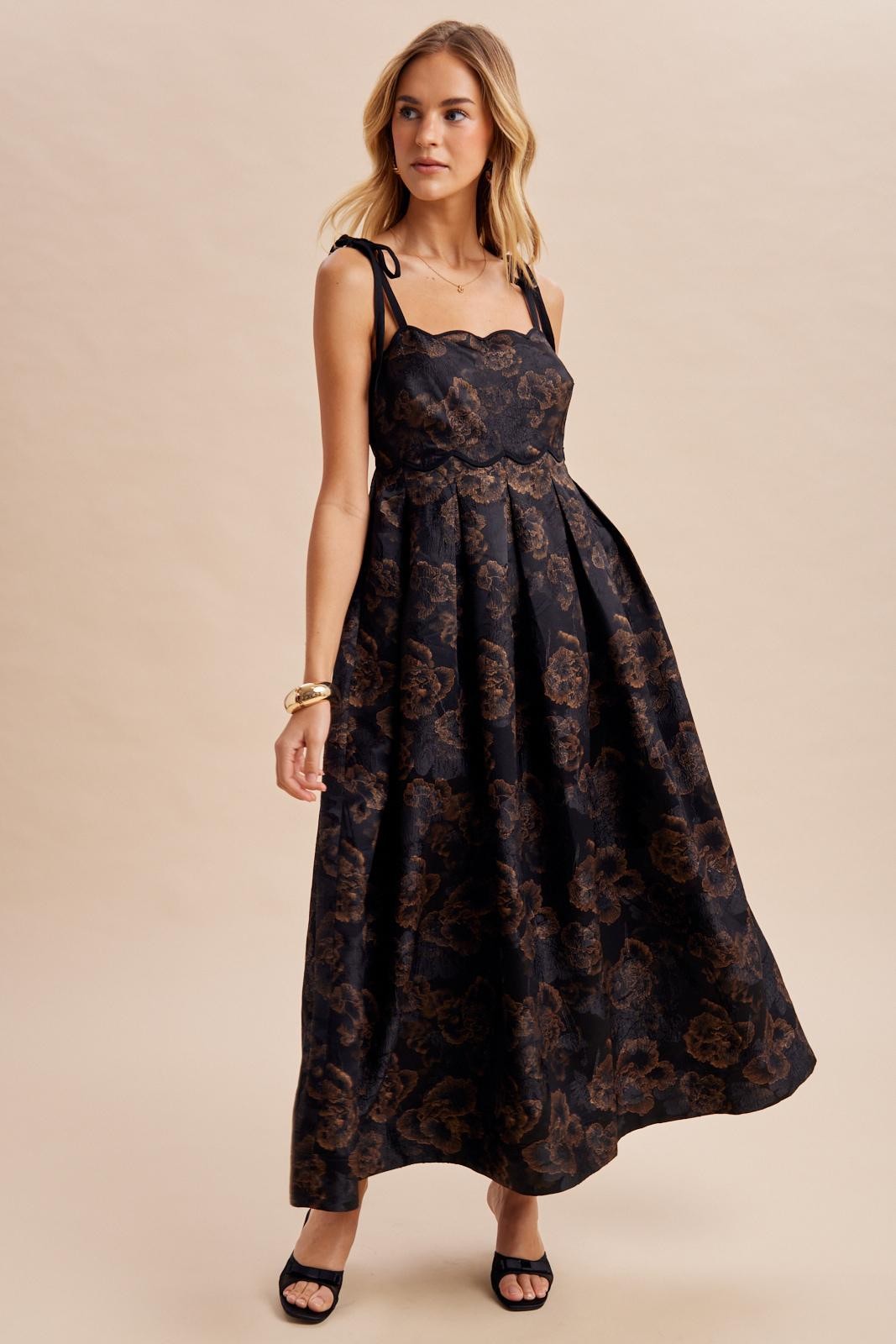 woman wearing a black maxi dress with a floral print and tie straps, styled with black heels