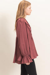 woman wearing a burgundy ruffled blouse with bell sleeves and a relaxed fit, paired with black leggings