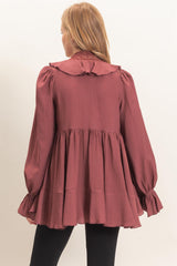 woman wearing a burgundy long sleeve peplum top with a ruffled collar and fitted cuffs, viewed from the back
