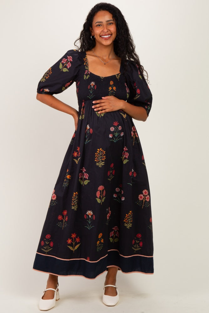 woman wearing a black floral maternity maxi dress and holding her baby bump