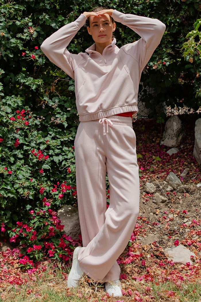 woman wearing a light pink long sleeve crop sweatshirt and matching wide-leg pants with a drawstring waist