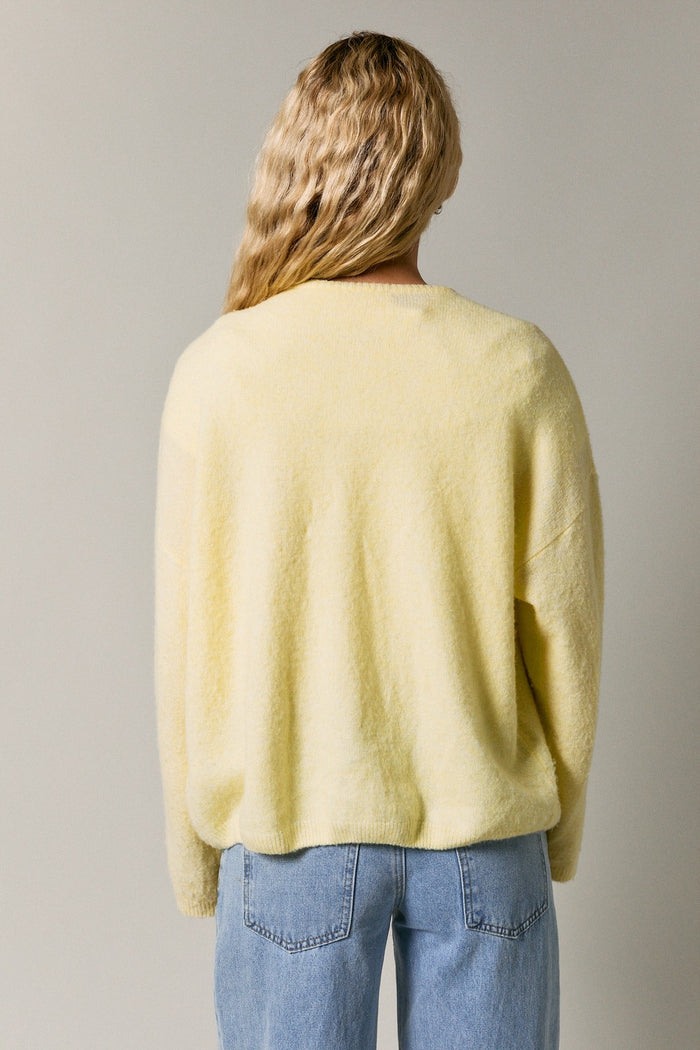 woman wearing a soft yellow oversized sweater seen from the back, paired with light blue jeans