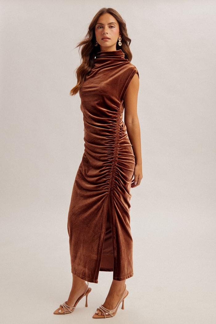 woman wearing a brown velvet maxi dress with ruching details and a high neck, styled with strappy heels
