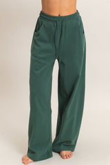 woman wearing dark green wide leg lounge pants with pockets and an elastic waistband