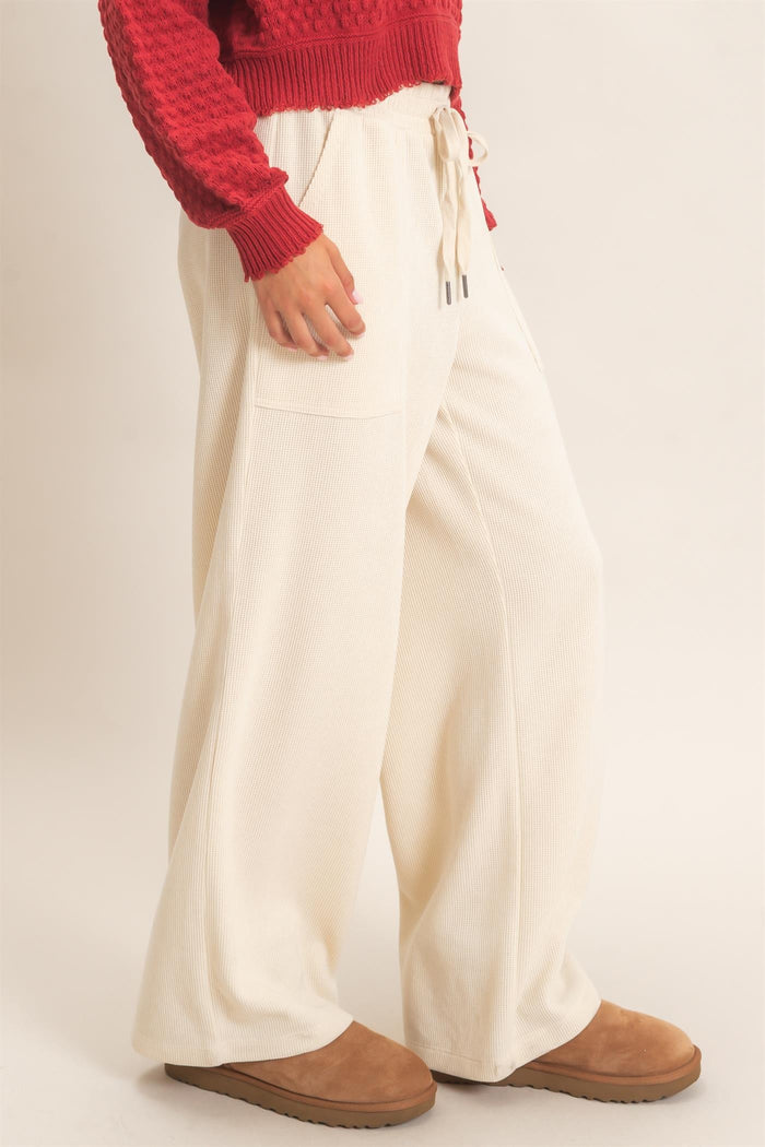 woman wearing cream wide-leg lounge pants with pockets and a drawstring waist, paired with a red textured sweater