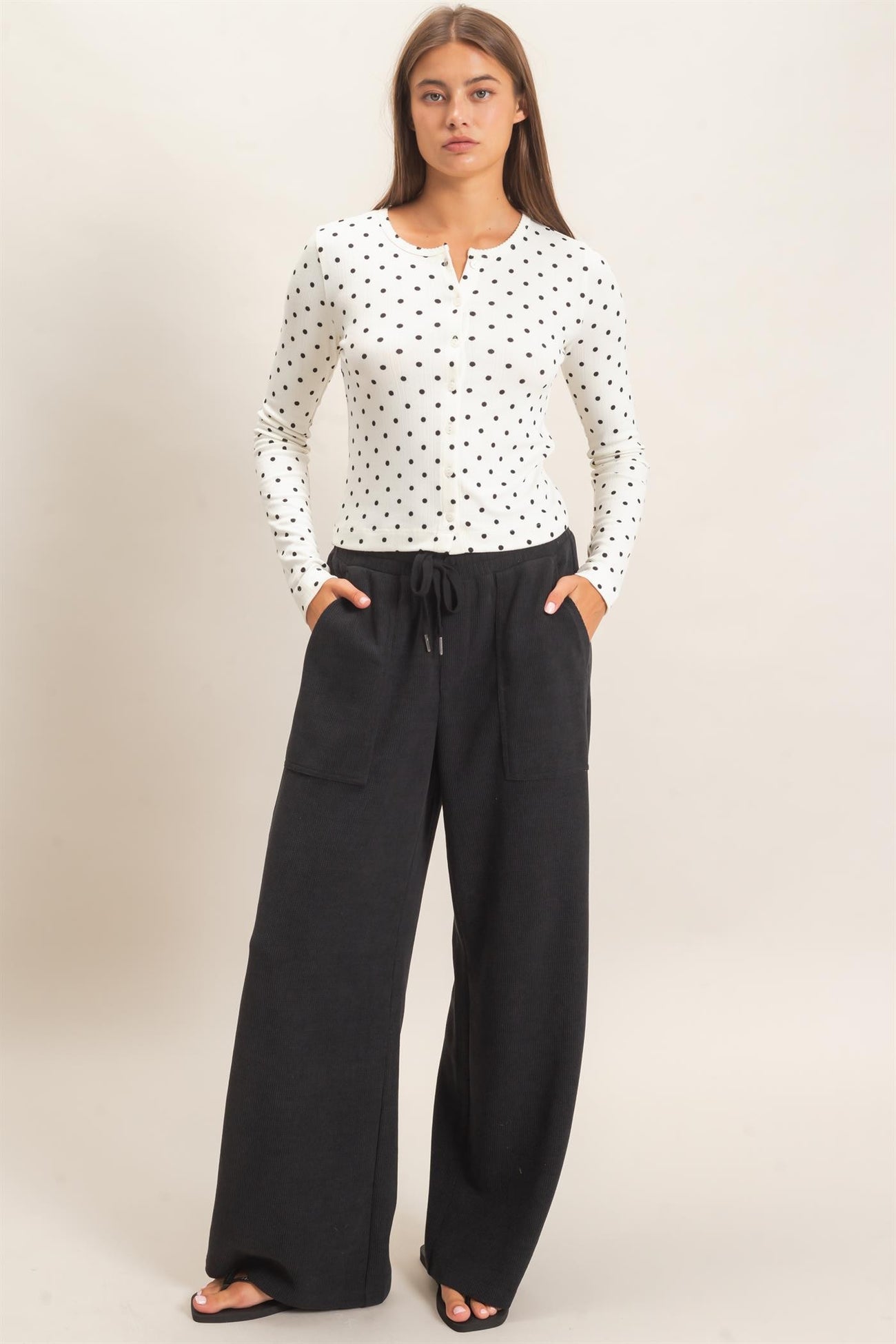 woman wearing a white polka dot long sleeve top and black wide-leg pants with pockets