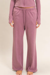 woman wearing a mauve loungewear set with long sleeve top and wide-leg pants, standing barefoot