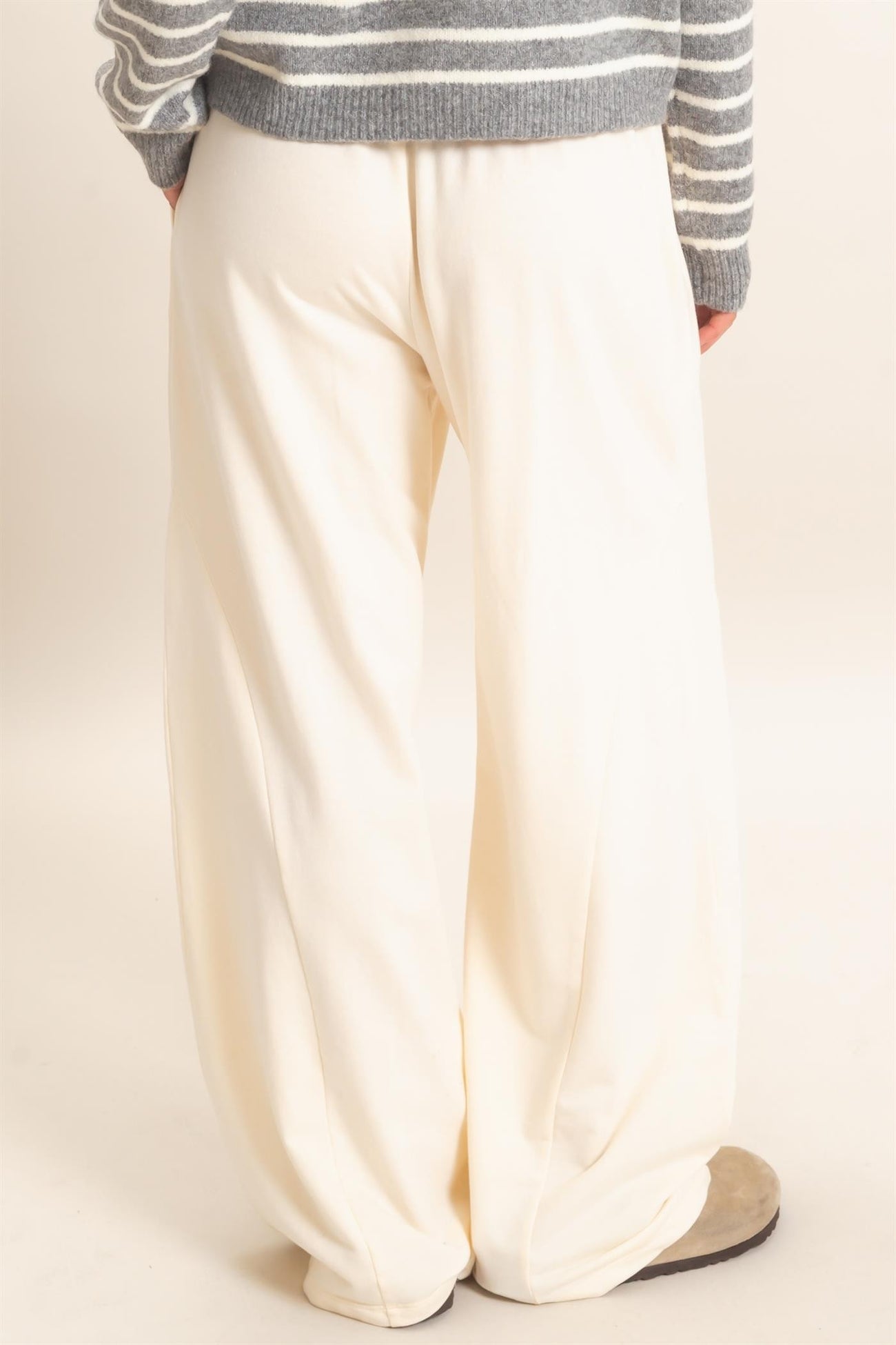 woman wearing white wide-leg pants, standing with her back to the camera, paired with a gray striped sweater