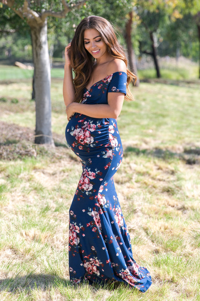 pregnant woman in blue floral off-the-shoulder maternity maxi dress standing in a park