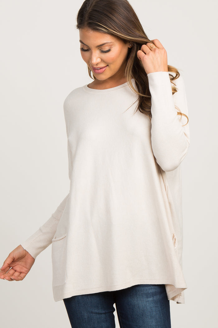 smiling pregnant woman wearing a cream long sleeve maternity tunic sweater and dark jeans