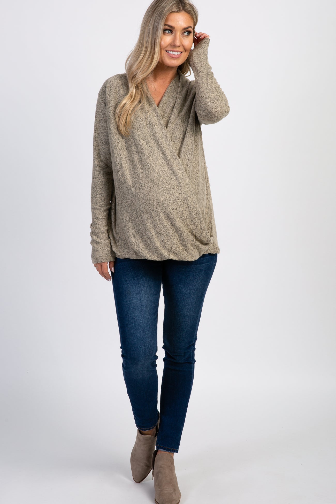 woman wearing a beige wrap maternity top and blue jeans, showing her baby bump with a casual look