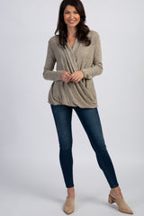 woman wearing a beige wrap-style long sleeve top with draped detailing and blue skinny jeans