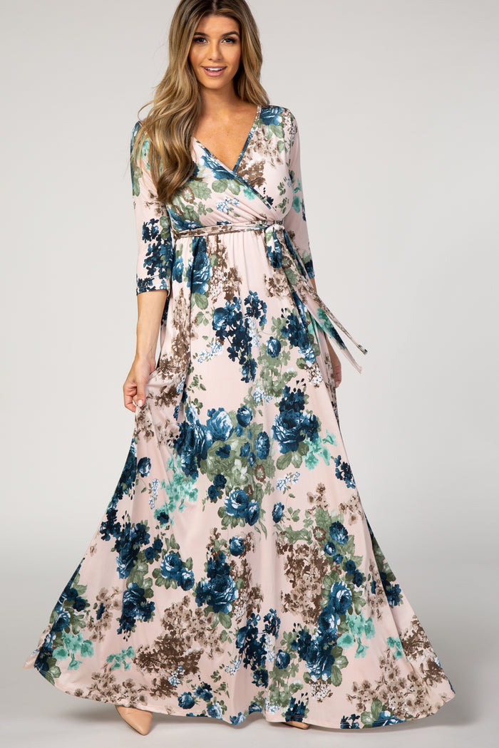 woman wearing a long floral wrap dress with shades of blue and green on a soft pink background.