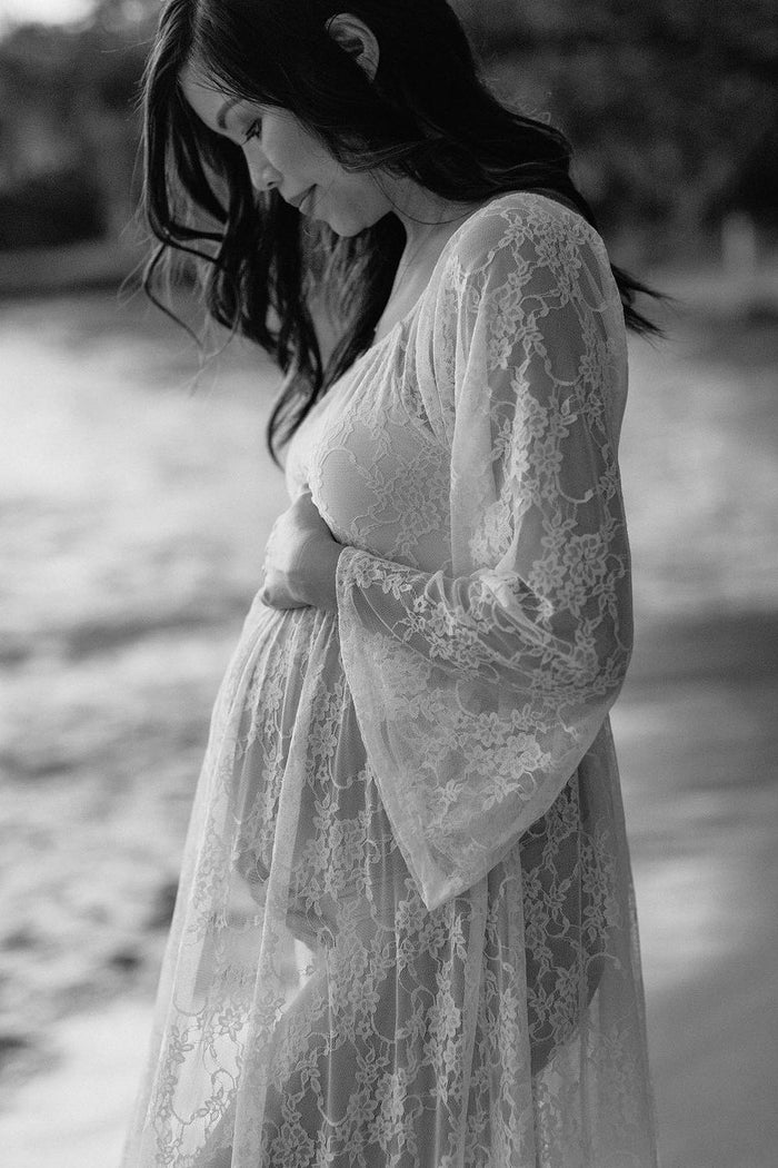woman wearing a sheer lace maternity robe, holding her baby bump by the water