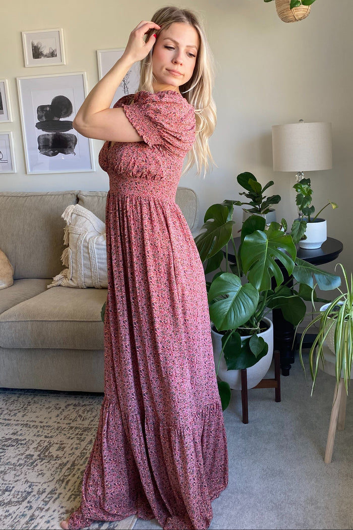 woman wearing a pink floral maxi dress with short sleeves and a tiered skirt, posing in a bright living room