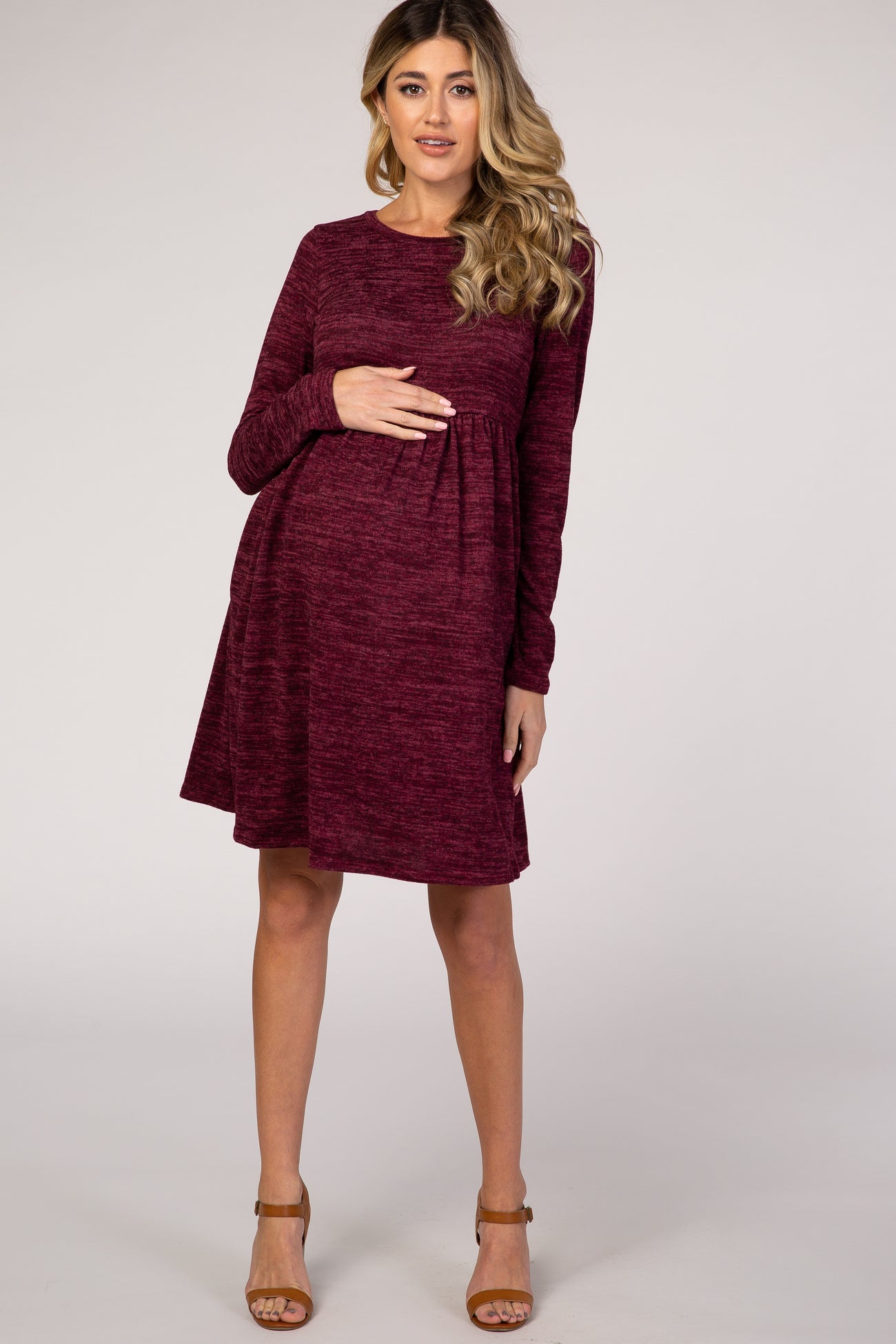 woman wearing a burgundy long sleeve maternity dress with a relaxed fit, holding her baby bump
