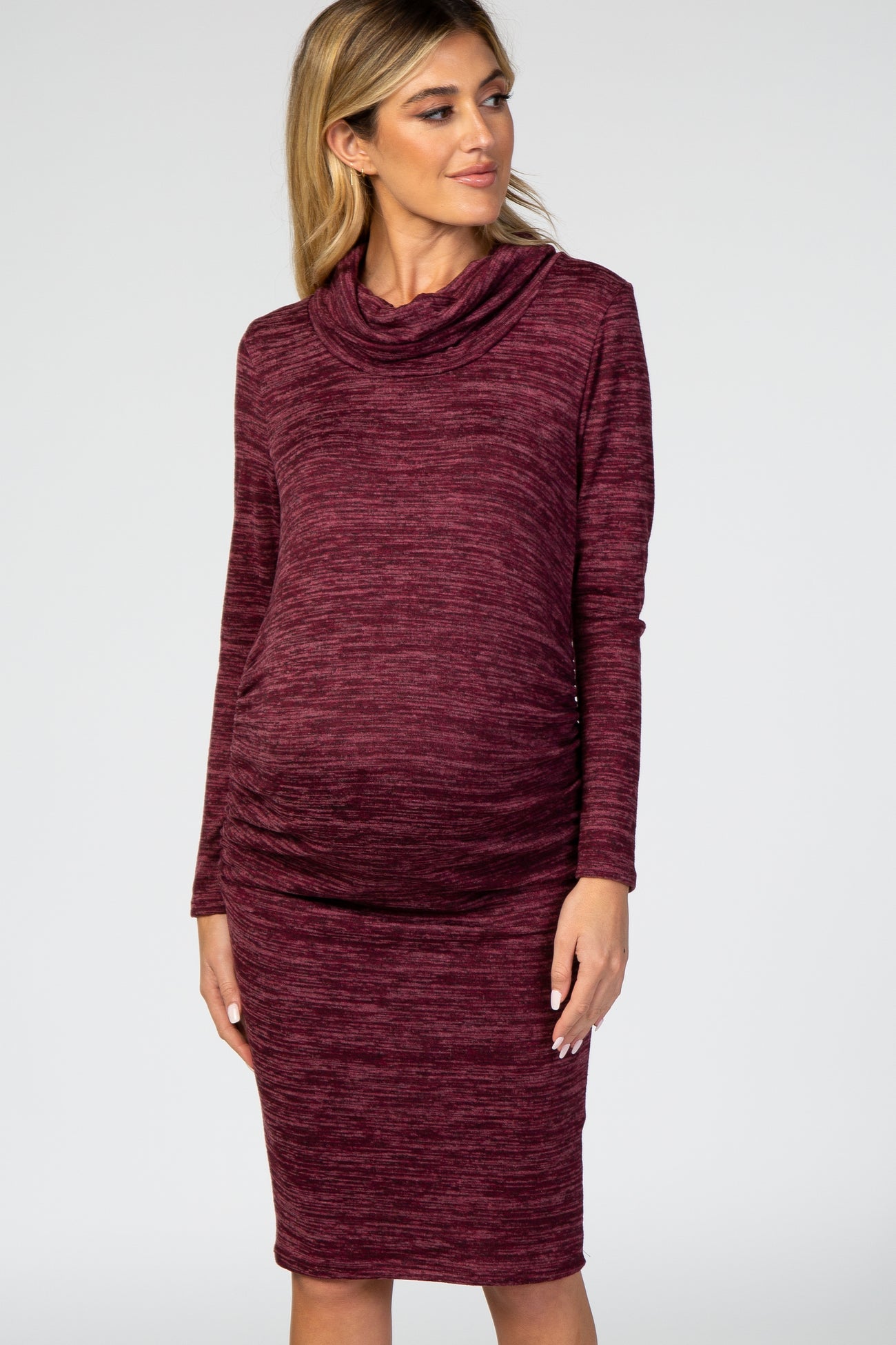 Pregnant woman wearing a burgundy cowl neck long sleeve knit maternity dress against a white background