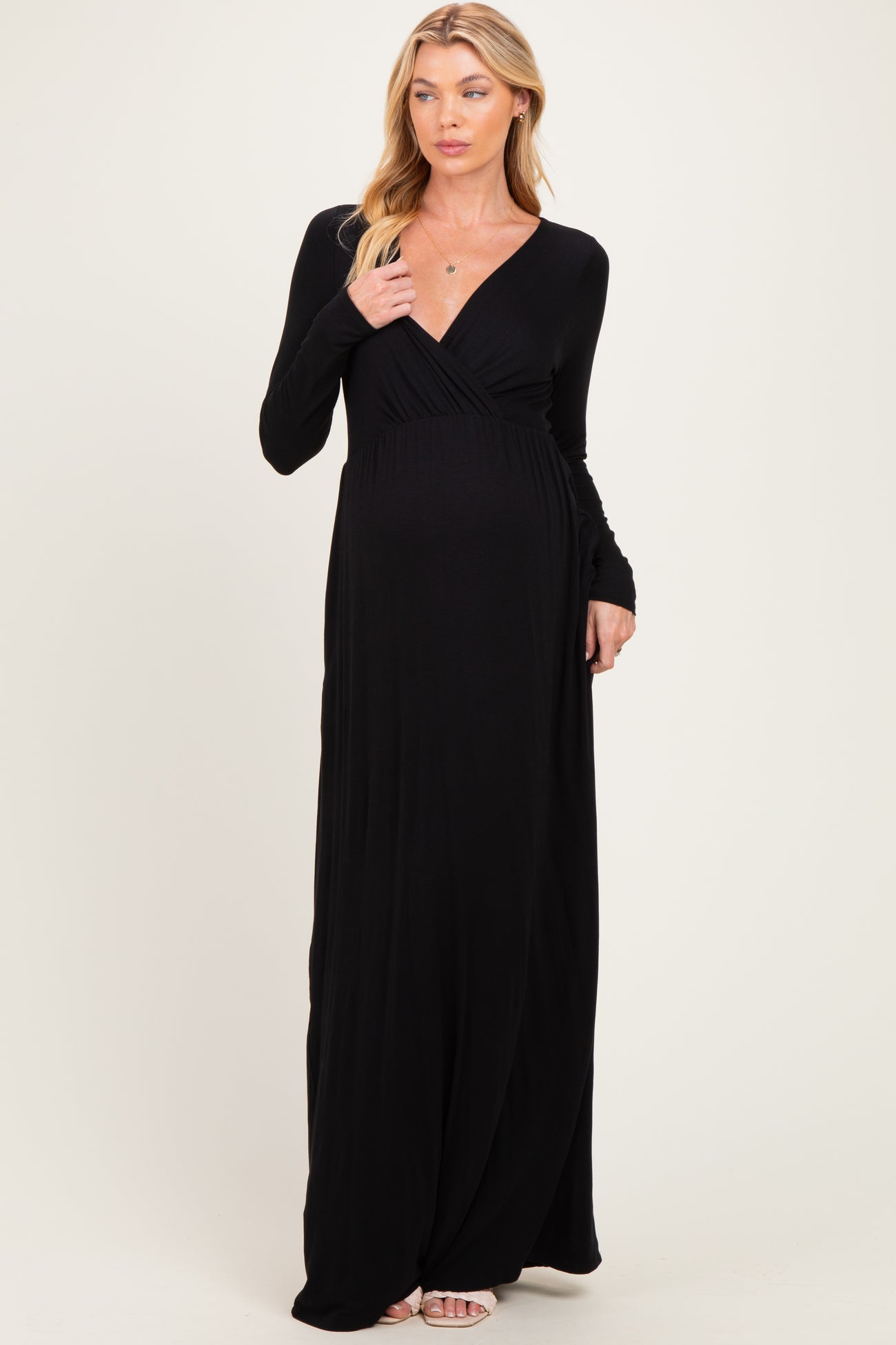 woman wearing a long black maternity dress with a deep v-neck and long sleeves, showcasing her baby bump