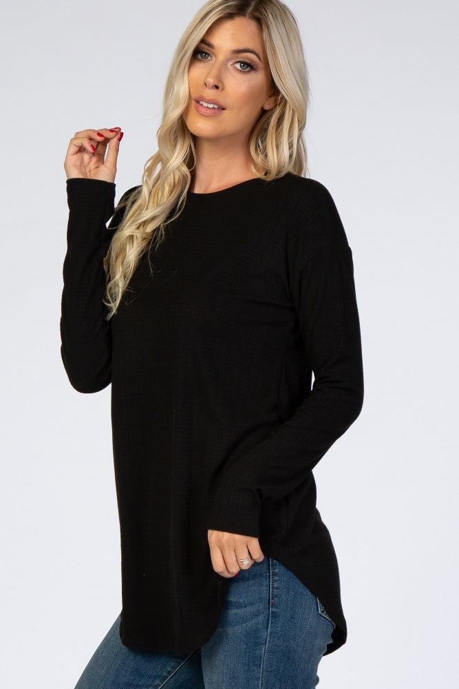 woman wearing a black long sleeve knit top with a relaxed fit and side slits, paired with blue jeans