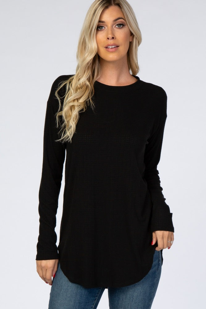 woman wearing a black long sleeve waffle knit top with a curved hem and relaxed fit, paired with blue jeans