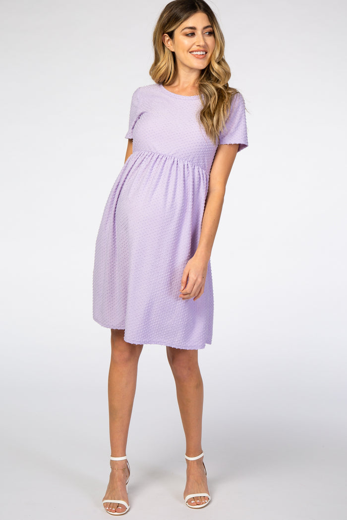 woman wearing a lavender short sleeve maternity dress with a textured pattern and a fitted waist, showing her baby bump