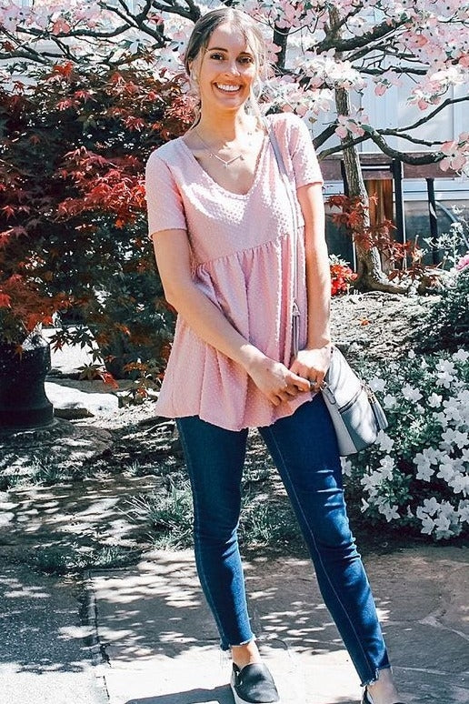 woman wearing a pink short sleeve peplum top paired with skinny jeans and a gray crossbody bag