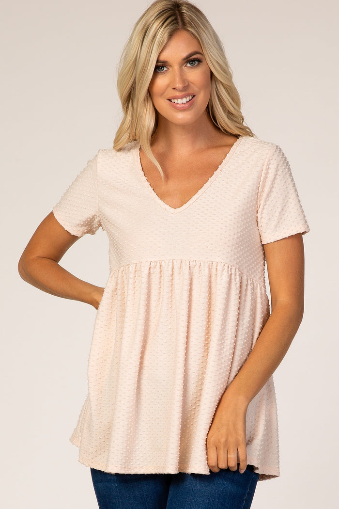 blonde woman wearing a light pink swiss dot v-neck maternity top with short sleeves and empire waist