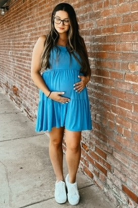 woman wearing a sleeveless light blue maternity dress and holding her baby bump