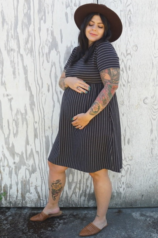 woman wearing a black and white striped maternity dress, holding her baby bump while standing outside