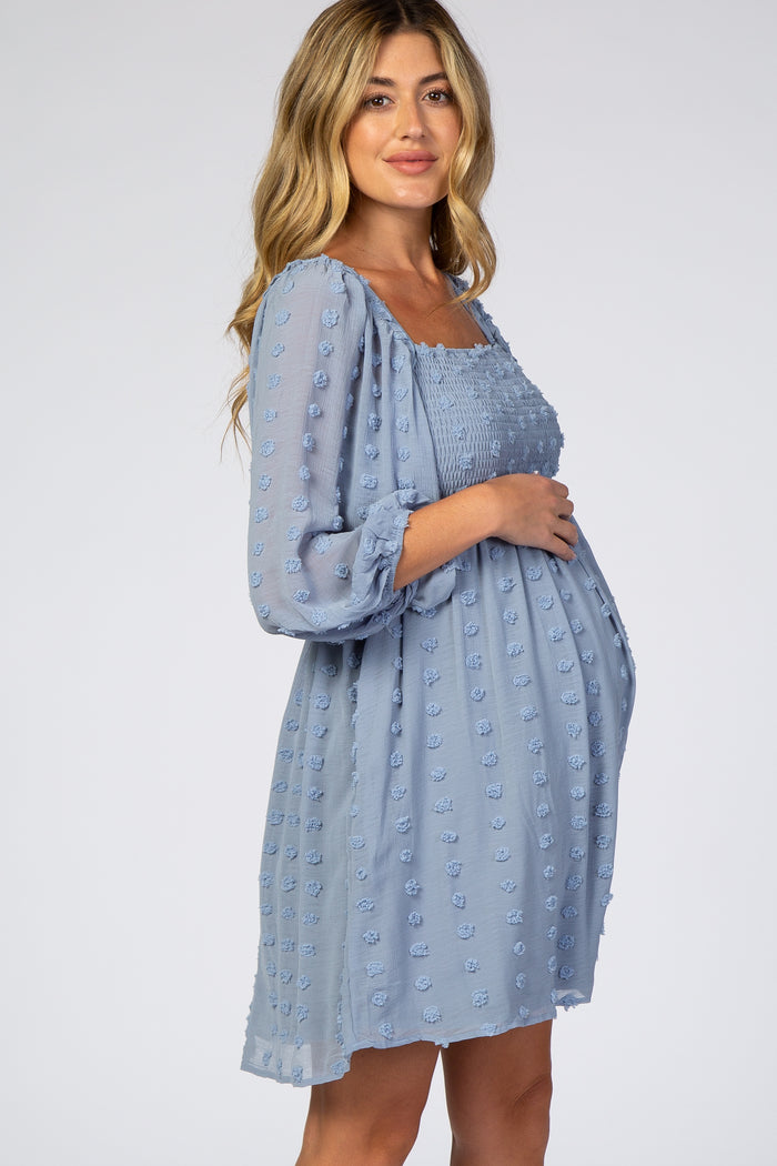 woman wearing a light blue maternity dress with textured dots and a smocked bodice, showcasing her baby bump
