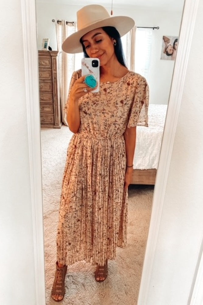 woman wearing a floral midi dress with short sleeves and a pleated skirt, paired with a wide-brimmed hat and strappy sandals