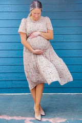 pregnant woman in floral maternity dress holding her baby bump against a blue wooden wall