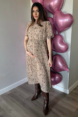 woman wearing a floral print maternity dress with pleats, holding her baby bump, standing in front of pink heart balloons