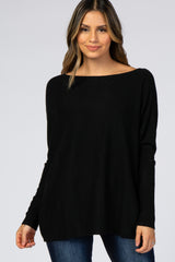 woman wearing a loose-fitting black sweater with an off-the-shoulder neckline and long sleeves, paired with denim jeans